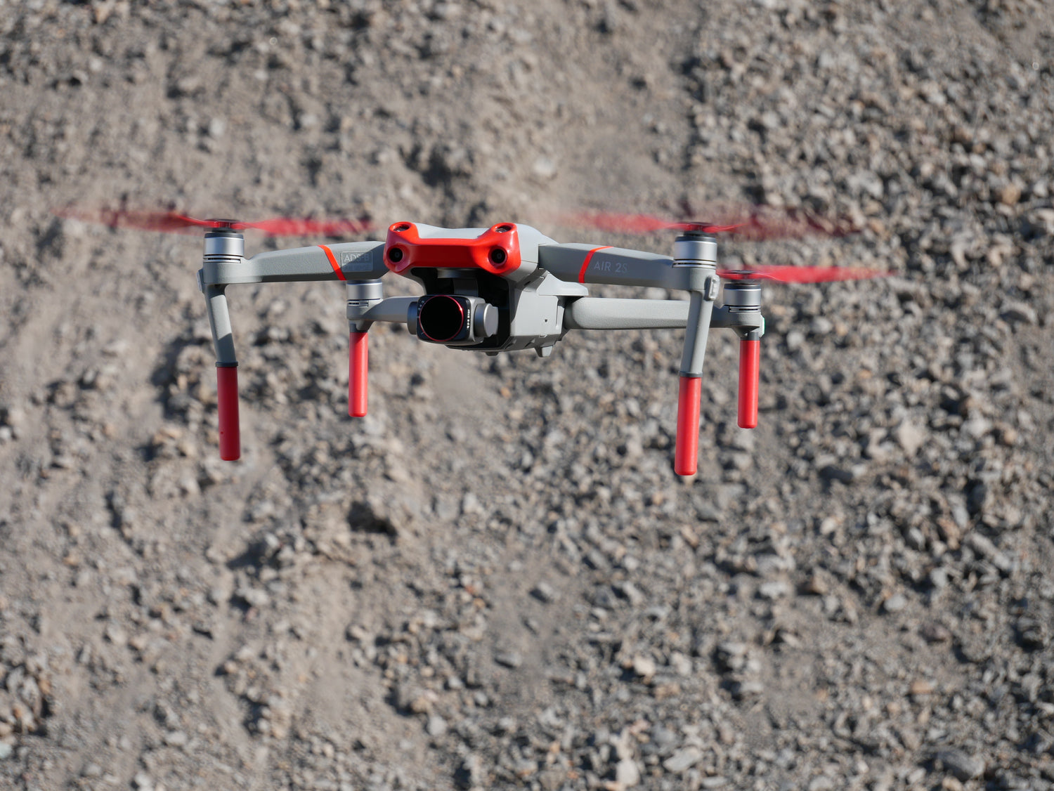 DJI Drohne mit Landegestell und roten Propellern vor einem steinigen Untergrund
